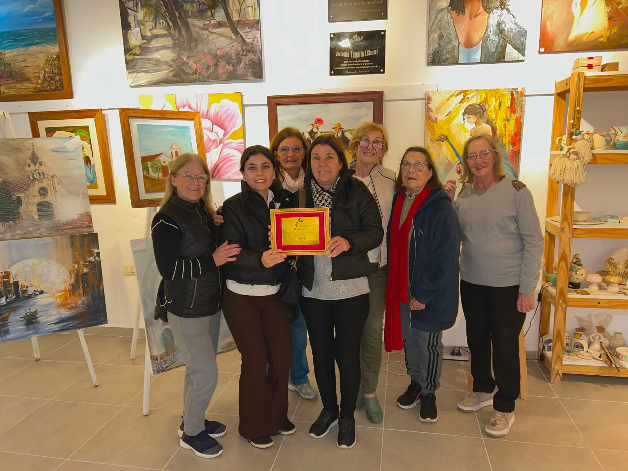Interior de la sala de la asociación: cuadros colgados en la pared, un caballete con una pintura y piezas de cerámica en los estantes.