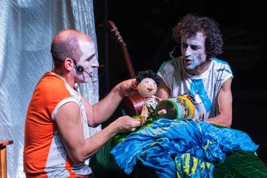 Dos intérpretes maquillados manipulan un títere junto a una guitarra sobre el escenario.
